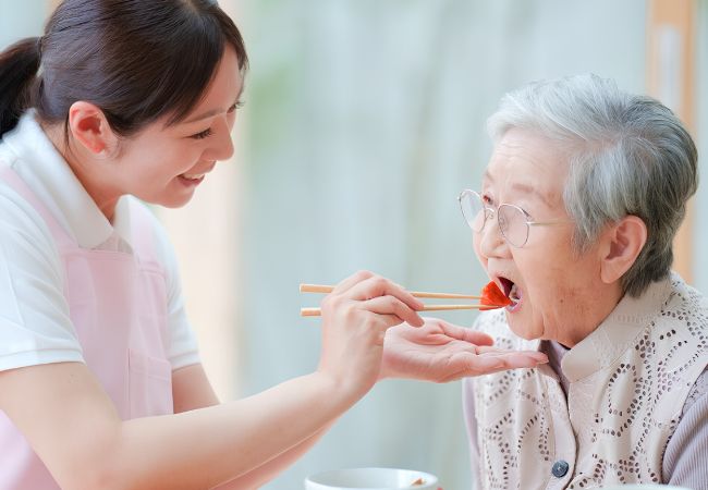 Người chăm sóc người cao tuổi hỗ trợ cụ bà ăn uống và chăm sóc sinh hoạt hằng ngày